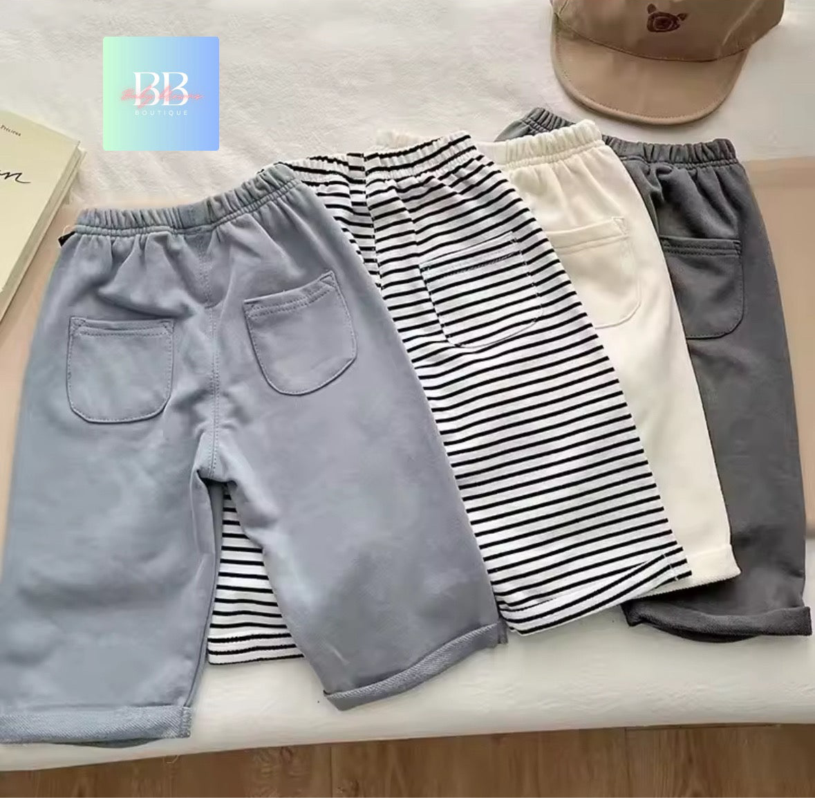 Four pairs of shorts in different colors and patterns on a surface with a brand logo in the corner.