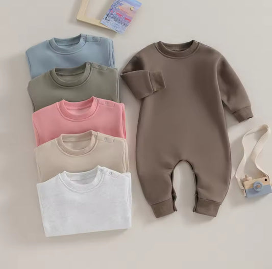 Collection of folded baby clothes including sweaters and a onesie on a light background