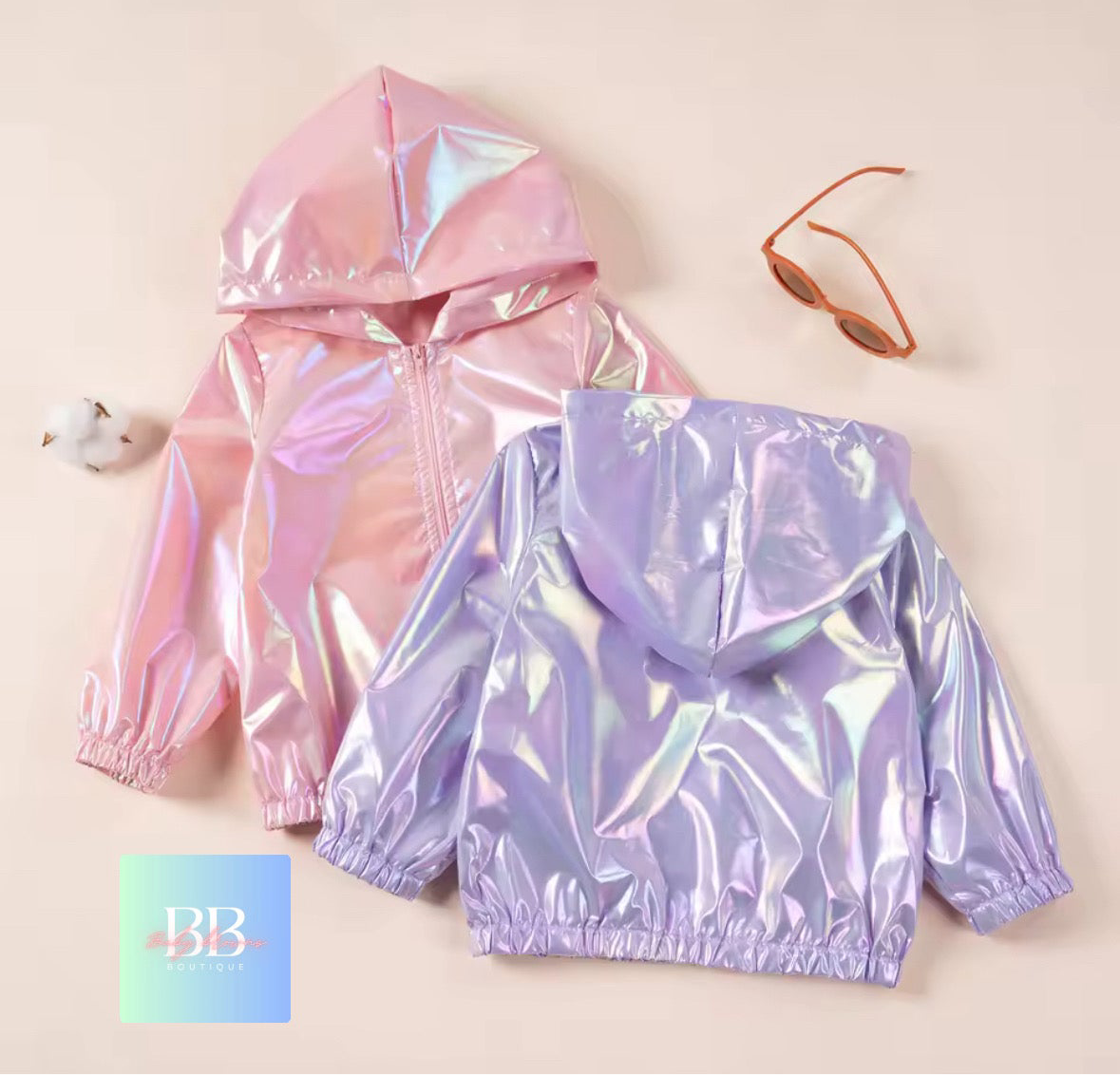 Two iridescent hoodies, one pink and one purple, on a beige background with sunglasses and a cotton ball.