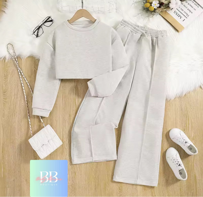 Light gray sweatshirt and pants set with white sneakers and handbag on a wooden surface.