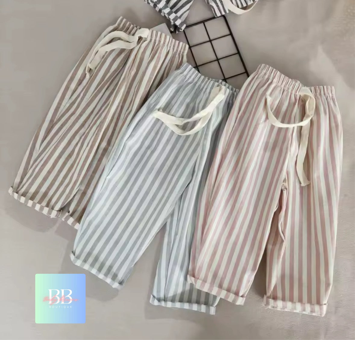 Three pairs of striped pants on a grid background with a brand logo in the corner.
