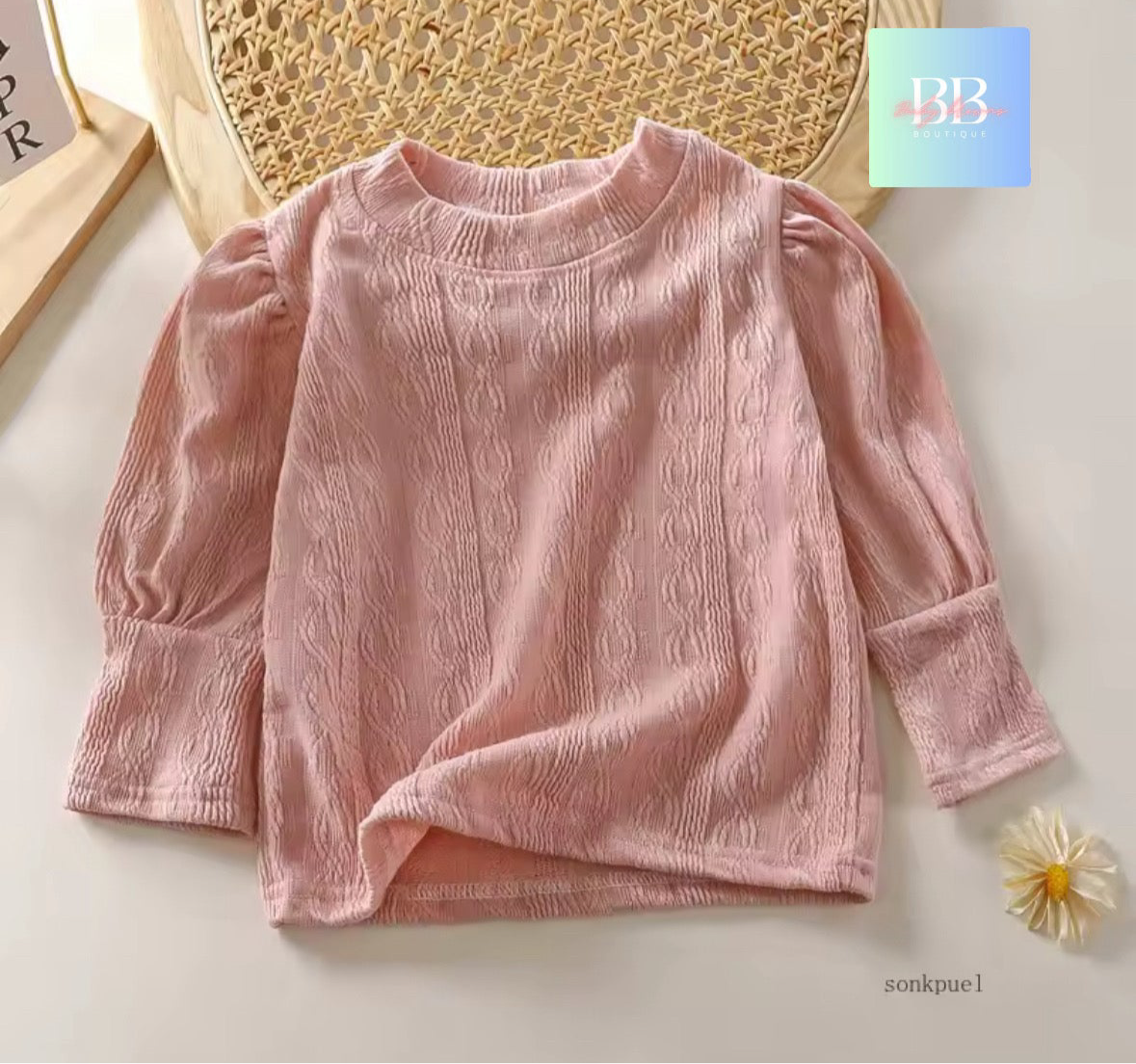 Pink textured sweater on a light background with a visible brand logo.