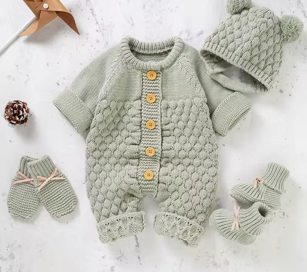 Knitted baby outfit with cardigan, hat, and socks on a light background
