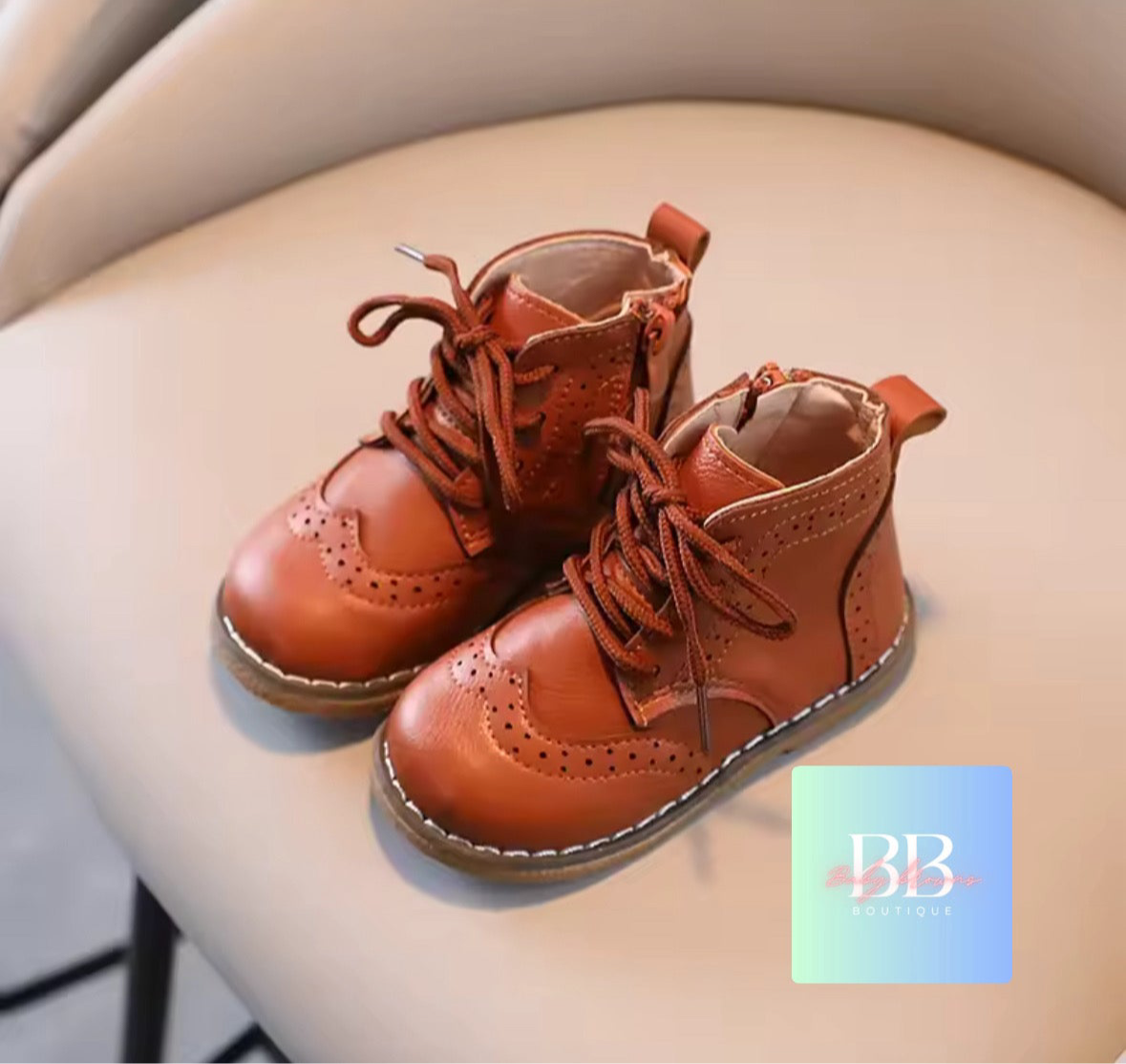 Pair of brown children's boots on a light-colored surface with a brand logo in the corner.