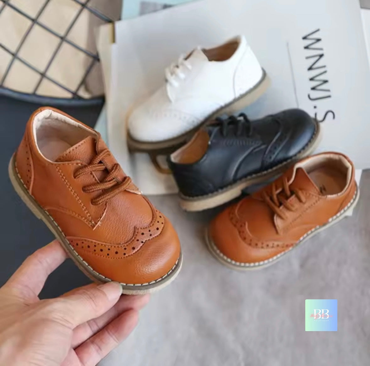 Pair of children's leather shoes in brown, black, and white on a textured surface.
