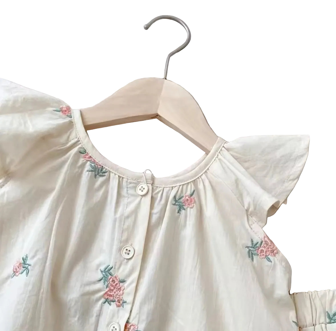 White blouse with floral embroidery on a hanger against a light gray background