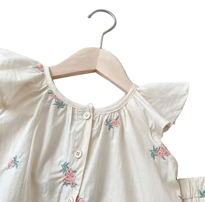 White blouse with floral embroidery on a hanger against a light gray background