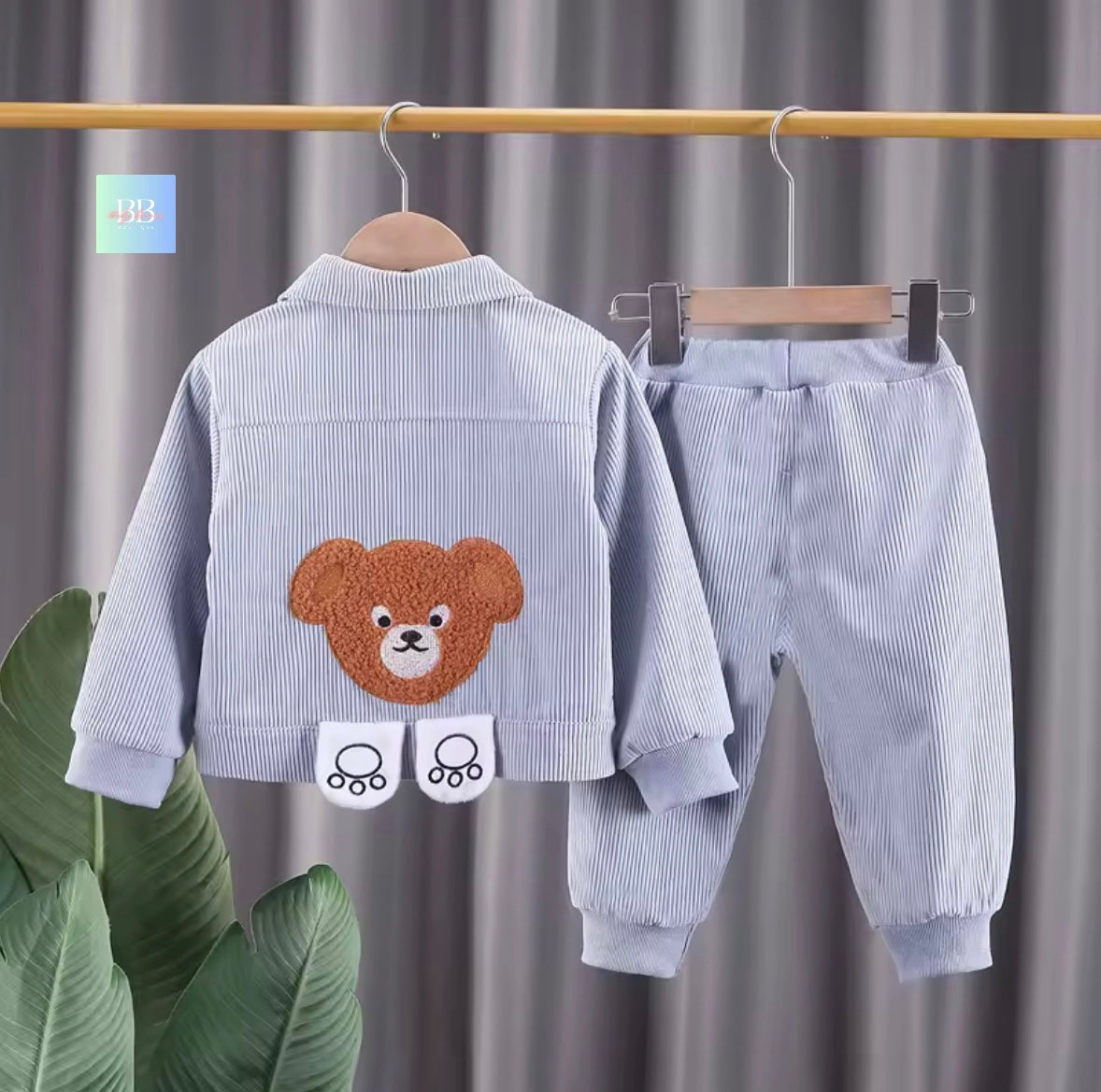 Children's blue corduroy outfit with bear design on a hanger against a gray curtain background.