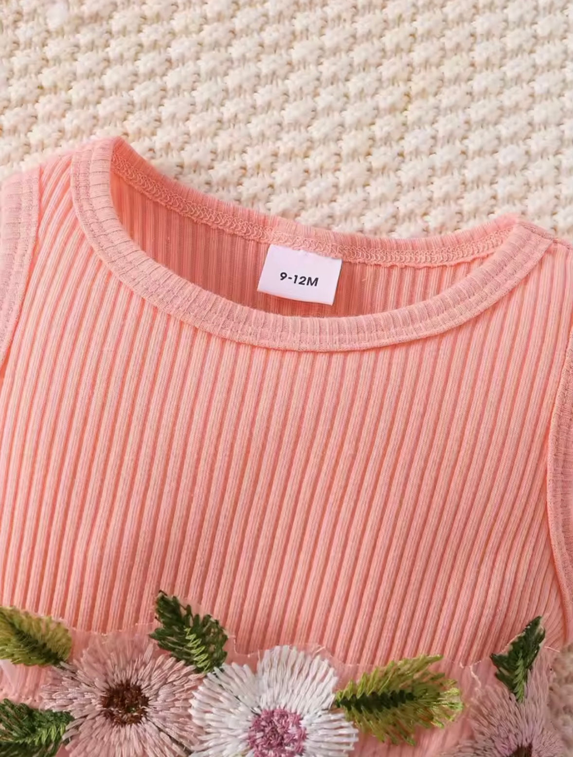 Pink ribbed sweater with floral and leaf patterns on a textured beige background