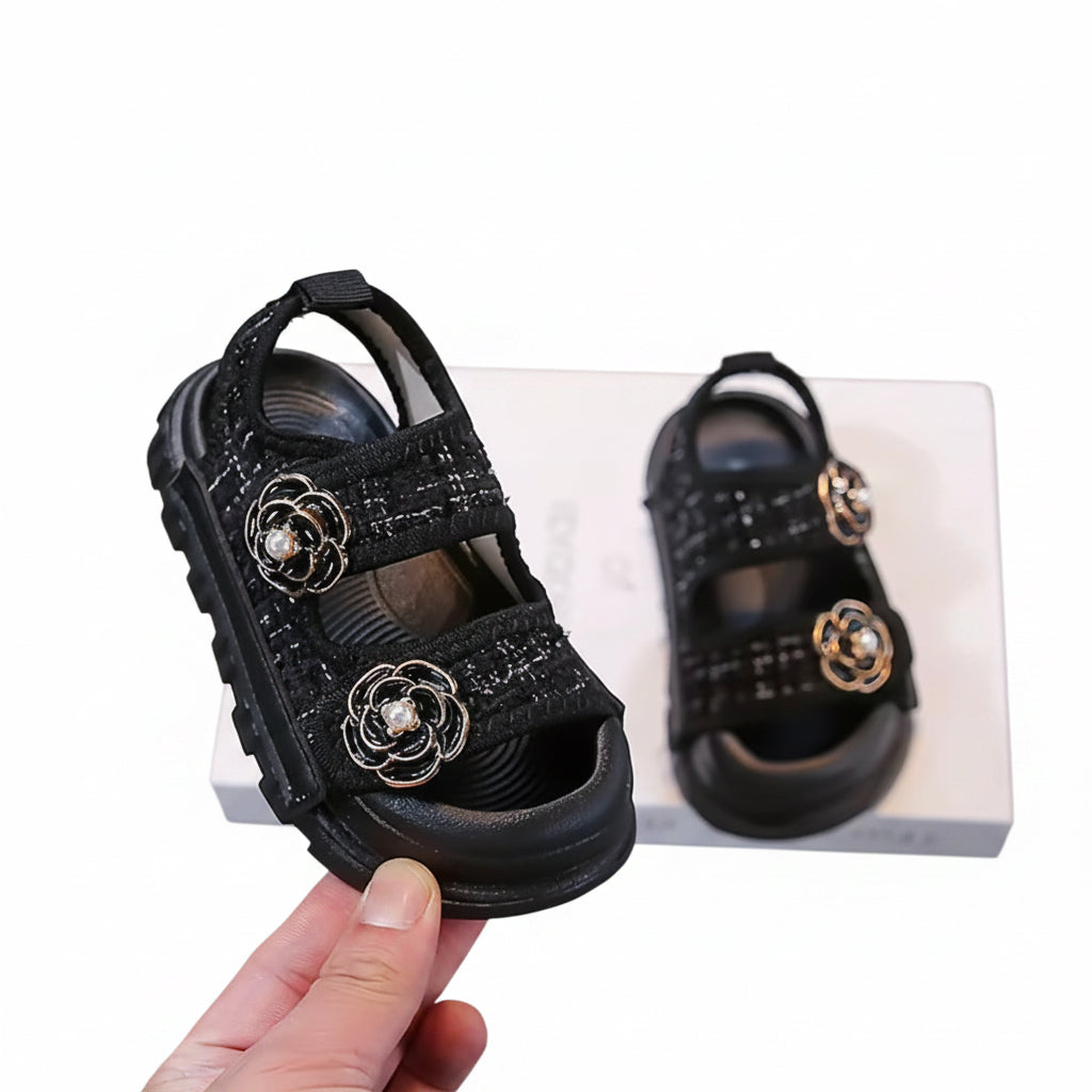 Black children's sandals with floral embellishments on a gray background