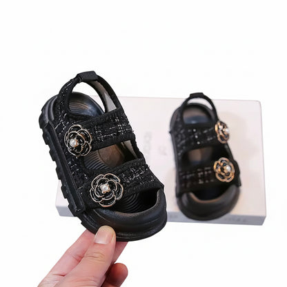 Black children's sandals with floral embellishments on a gray background