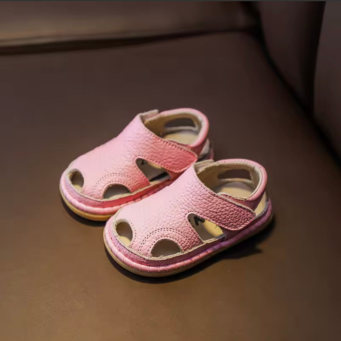 Pair of pink children's sandals on a brown surface
