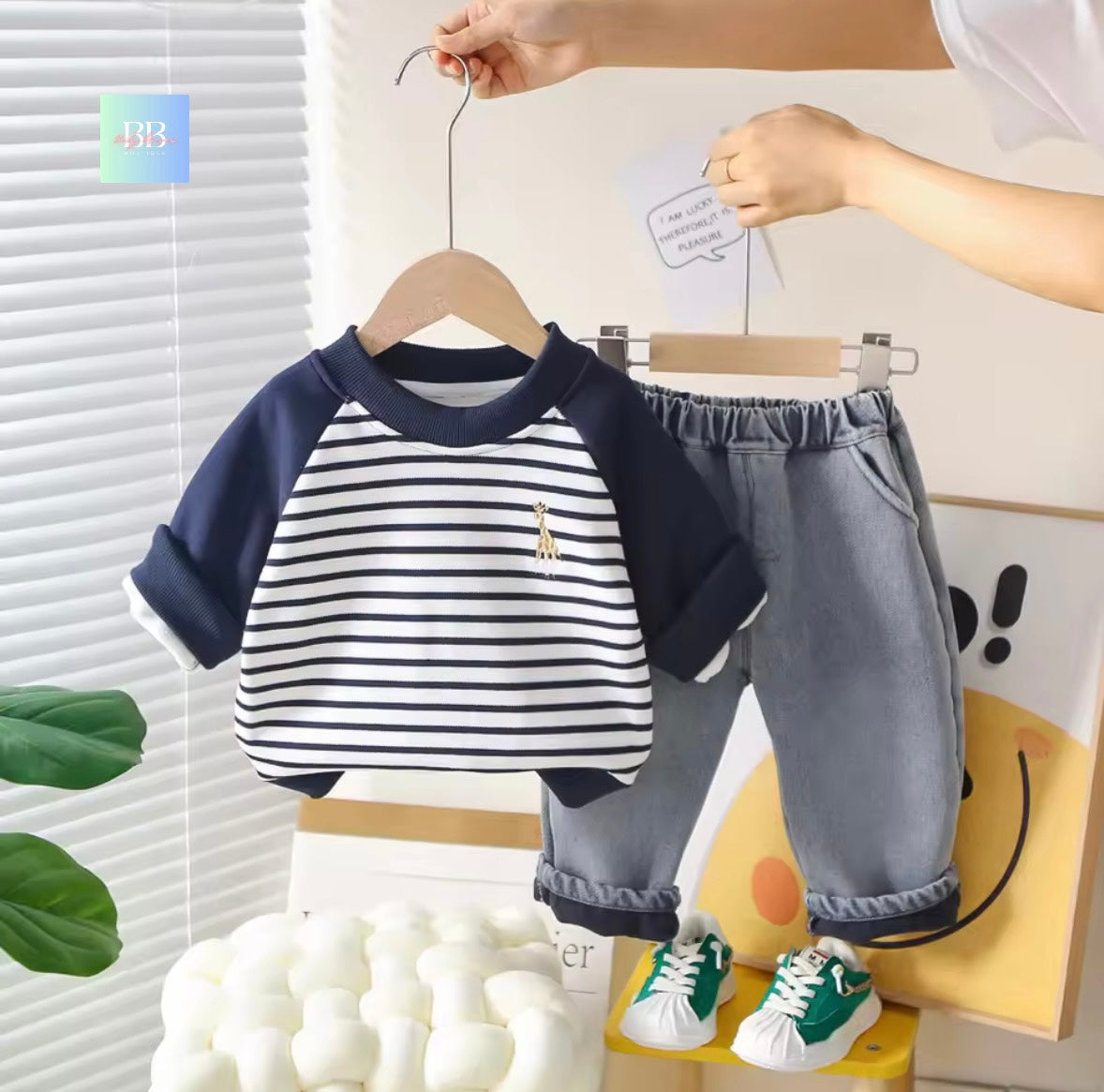 Children's outfit with striped shirt and gray pants on a hanger against a light background.