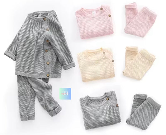 Collection of baby clothing including a gray cardigan, pants, and shirts on a white background.