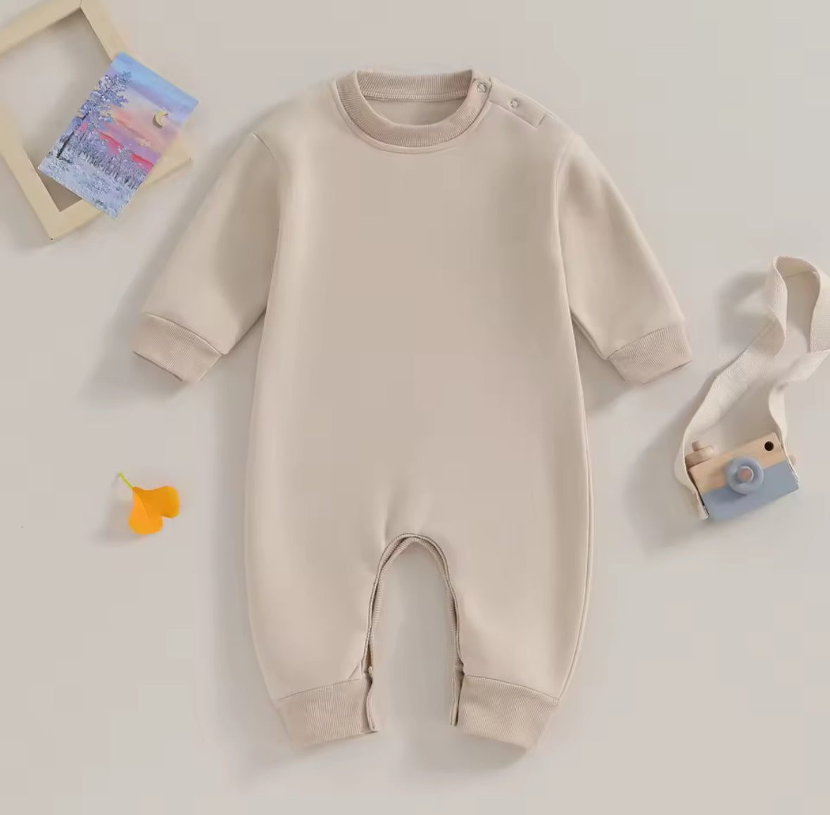 Beige baby onesie on a light gray background with toys around
