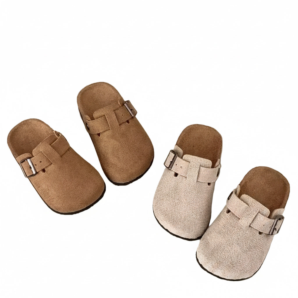 Pair of brown and beige slippers on a light surface with a wooden shelf in the background.