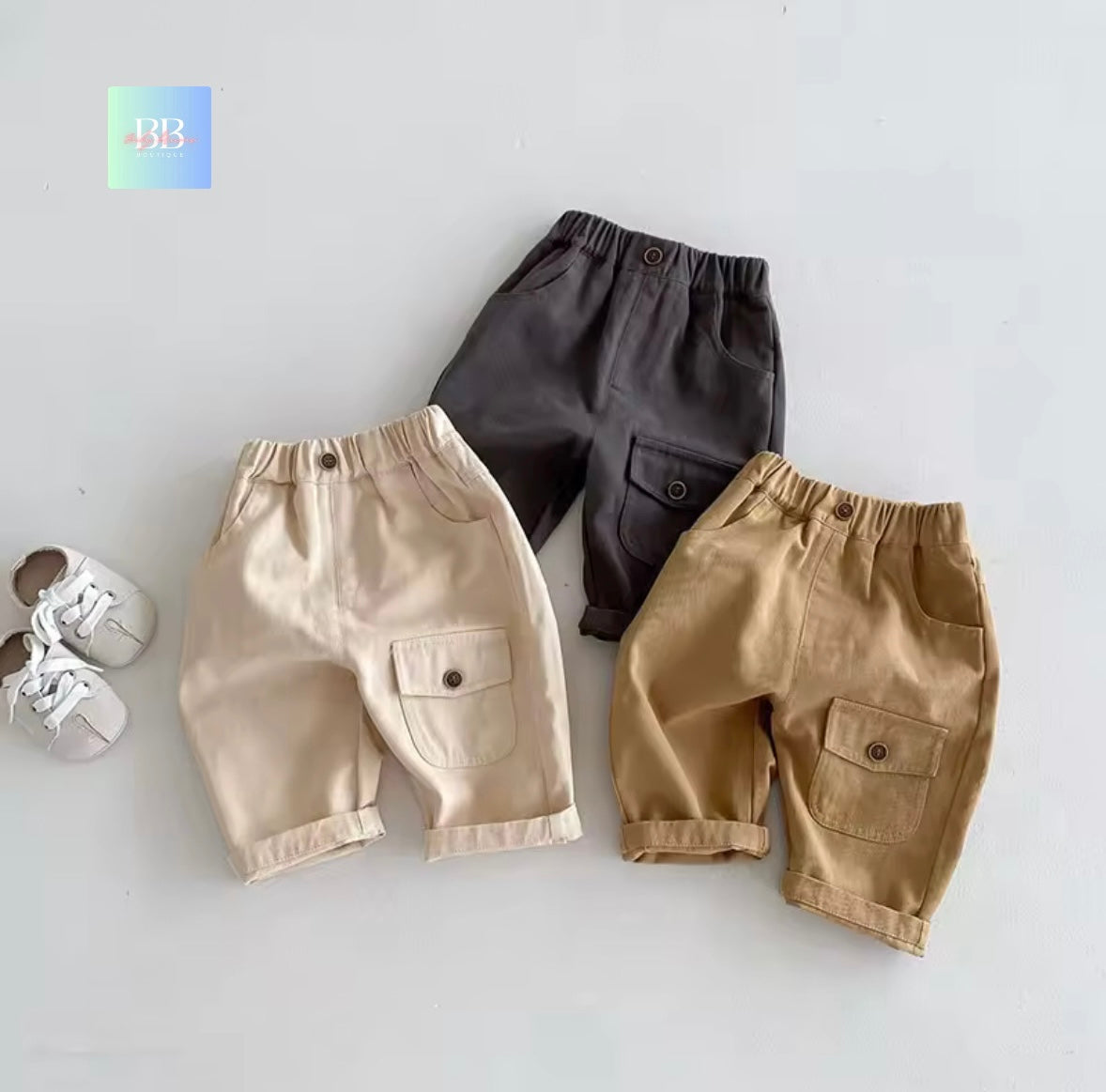 Three pairs of children's pants in beige, black, and brown on a light gray background.