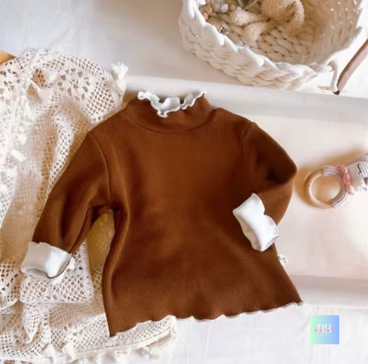 Brown sweater with white cuffs and collar on a lace surface