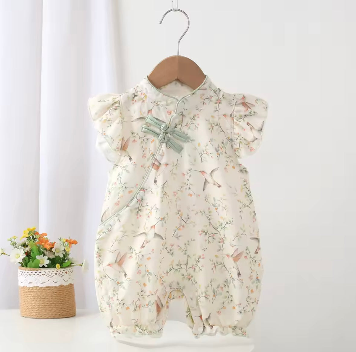 Floral baby romper on a hanger against a white background