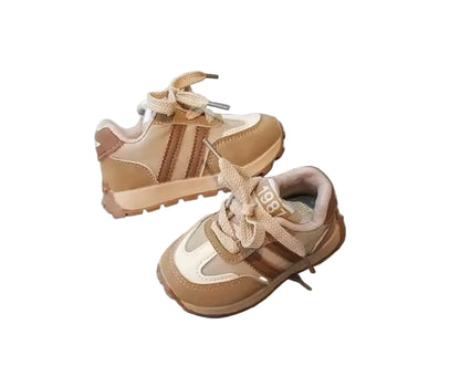 Pair of beige and brown children's sneakers on a light gray surface