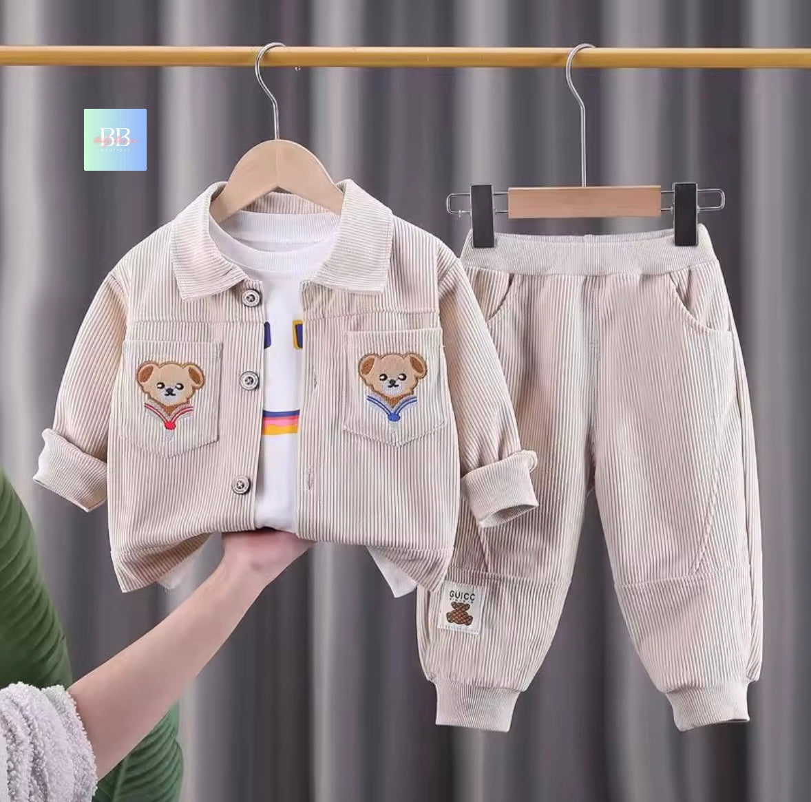 Children's corduroy outfit with teddy bear designs on a hanger against a gray curtain background.