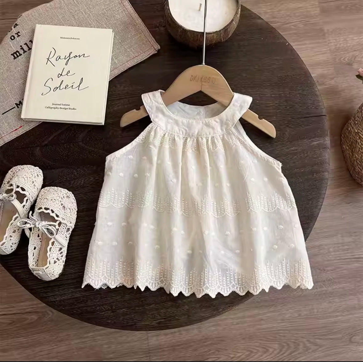 White lace dress on a wooden hanger with white shoes and a book on a wooden surface