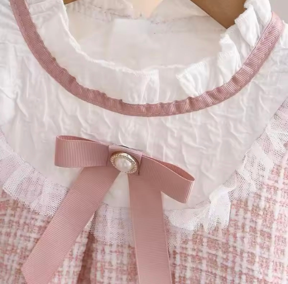 Close-up of a white lace garment with a pink ribbon and button detail.