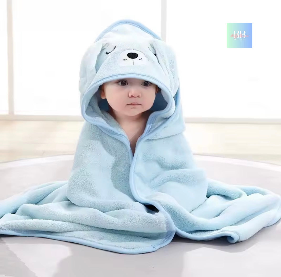 Child wrapped in a blue hooded towel with bear design on a light background
