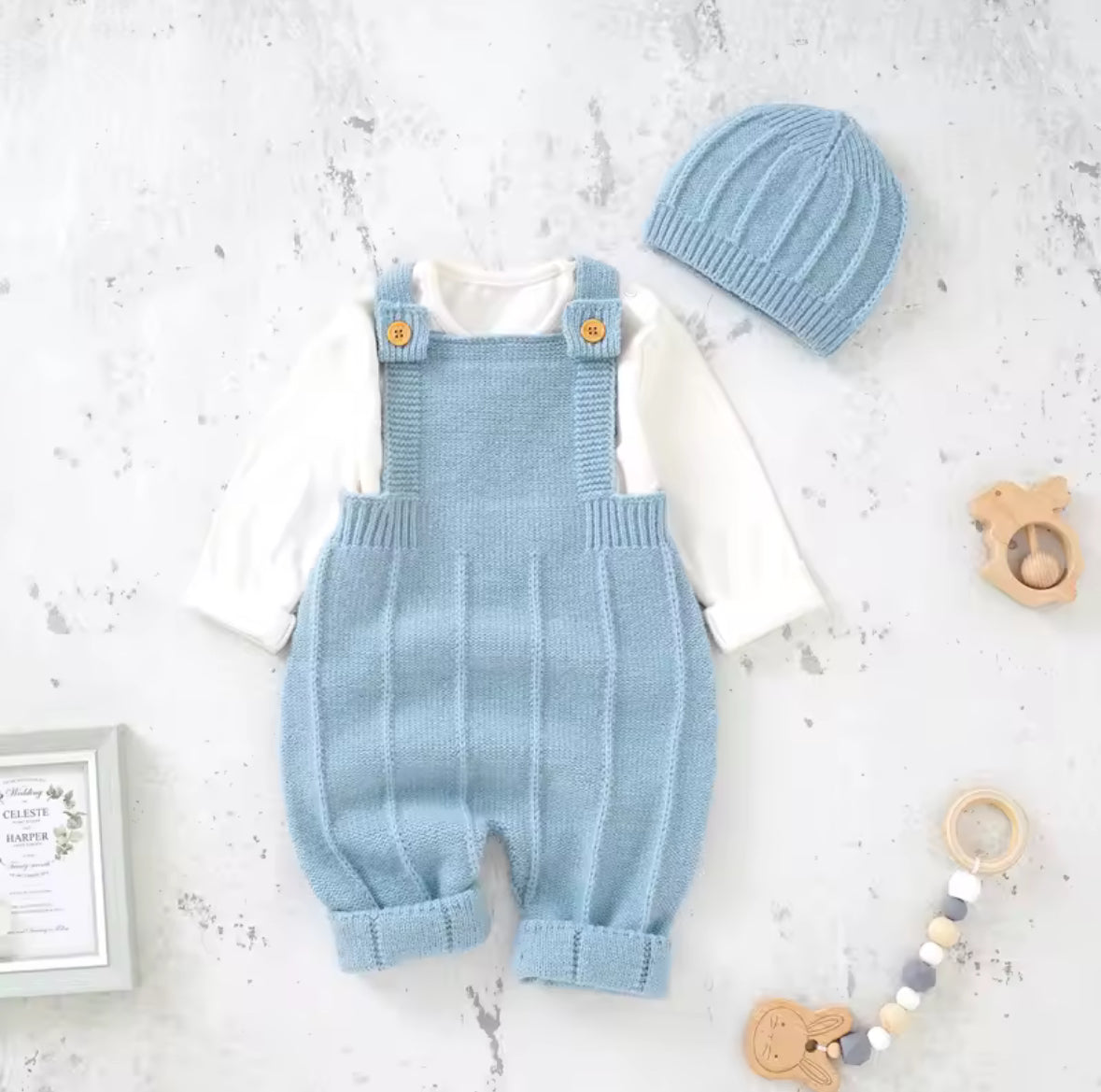 Light blue knitted romper with matching hat on a white surface with toys around