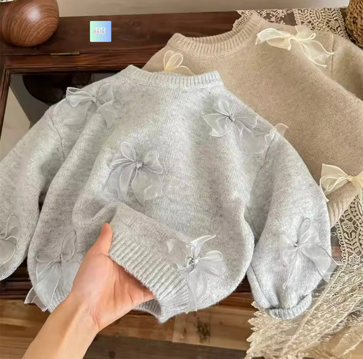 Light gray sweater with floral details held by a hand on a wooden surface.