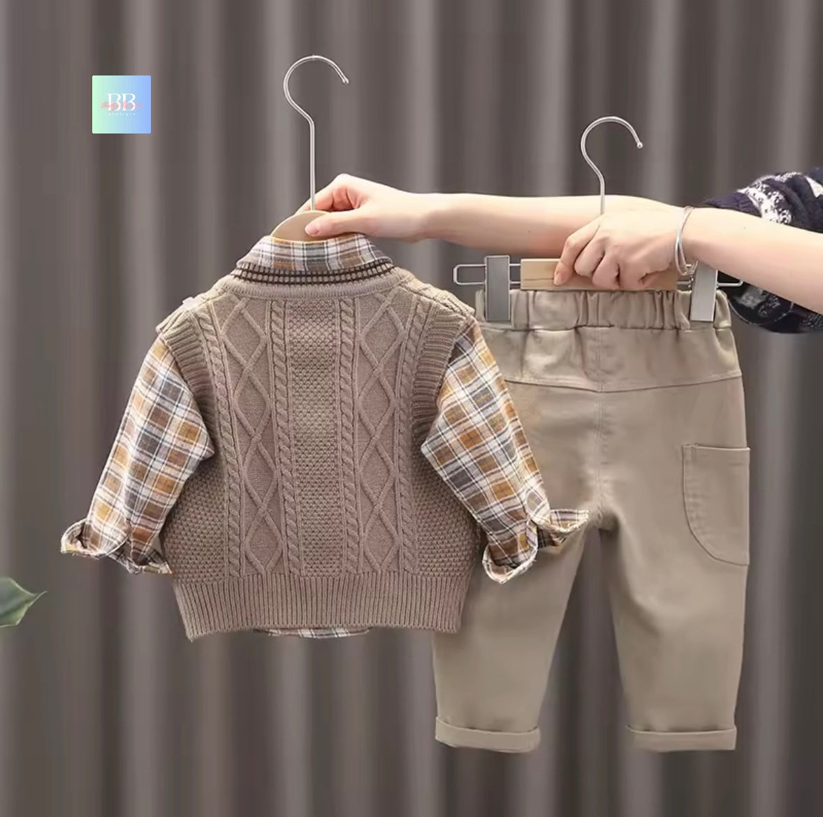 Children's clothing set with sweater and pants on hangers against a neutral background