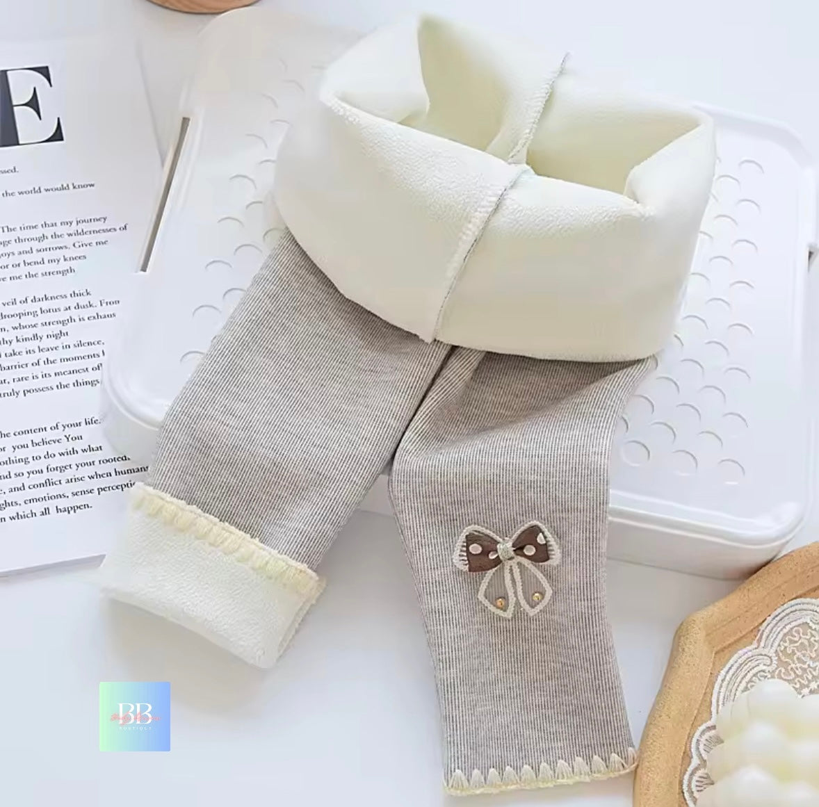 Gray baby pants with white cuffs and a butterfly patch on a white surface.