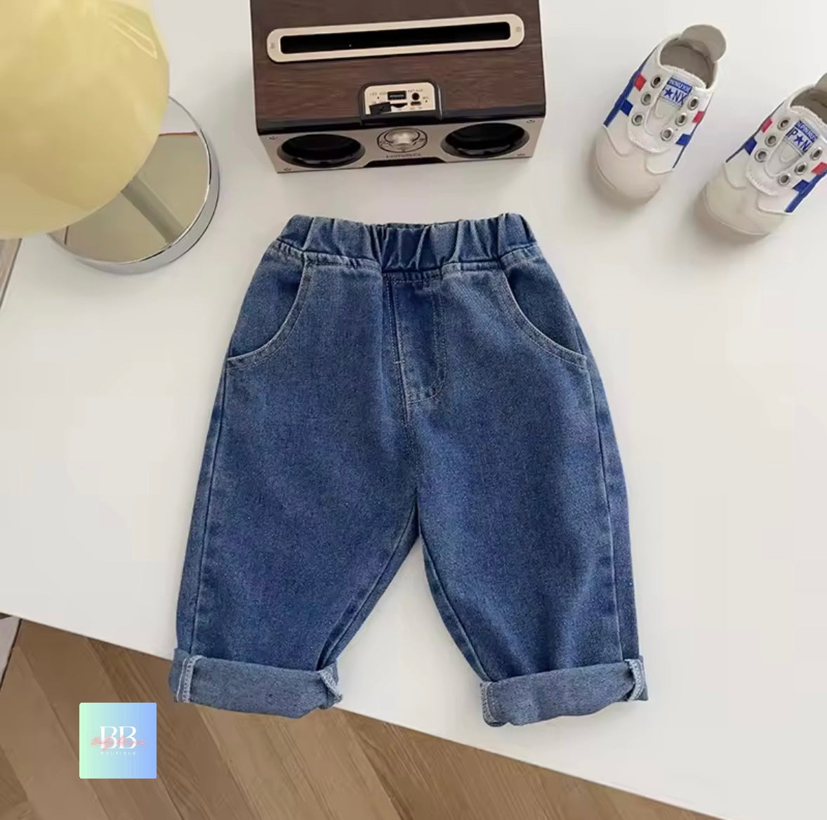Blue jeans on a white surface with a small radio and shoes in the background
