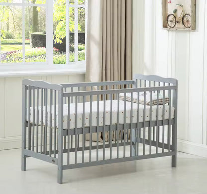 Gray crib with white mattress in a room with a window and curtains.