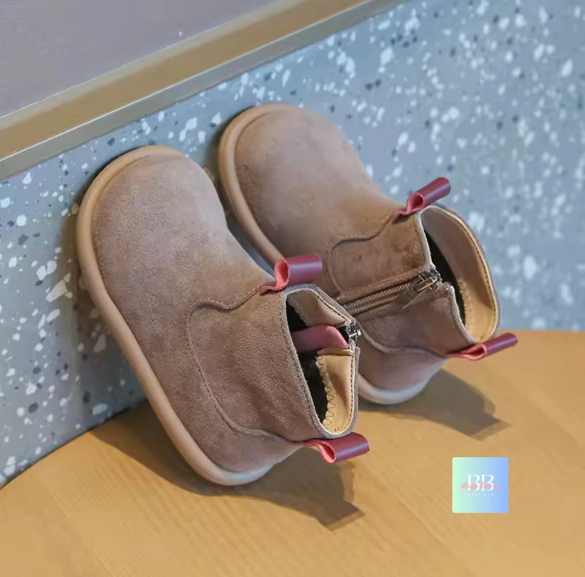 Pair of brown children's boots with pink straps on a wooden surface.
