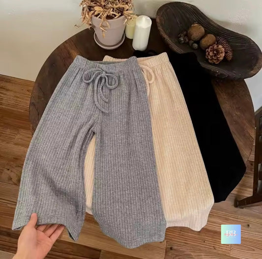 Two pairs of ribbed knit pants, one gray and one beige, on a wooden table.