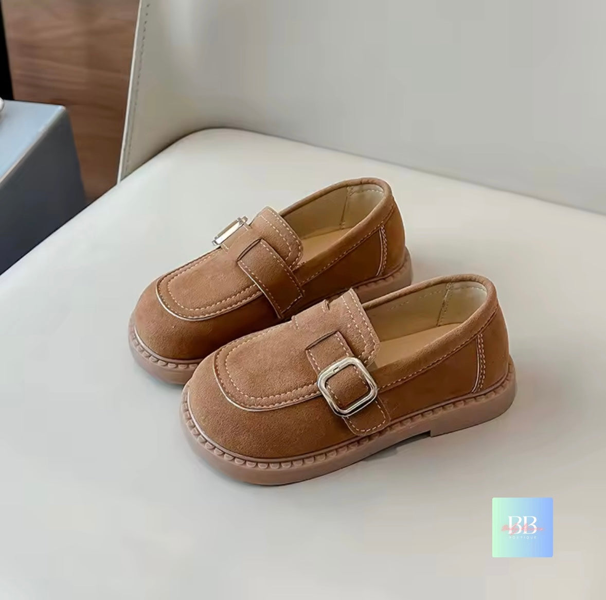 Pair of brown children's shoes with buckles on a light-colored surface.