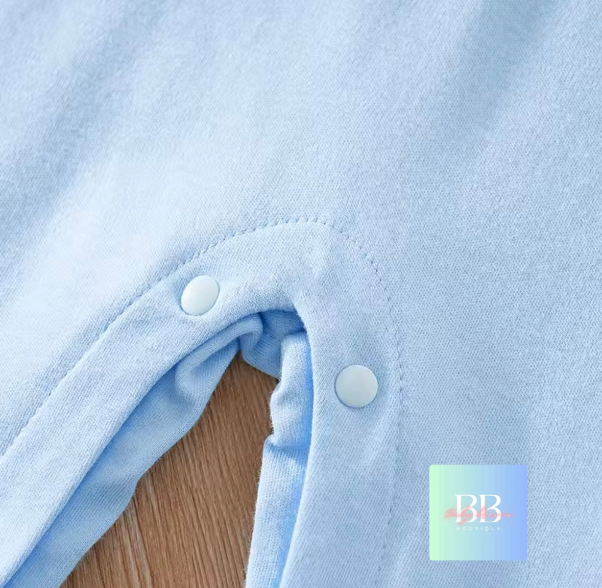 Close-up of a light blue garment with buttons on a wooden surface, featuring the brand 'BB'.