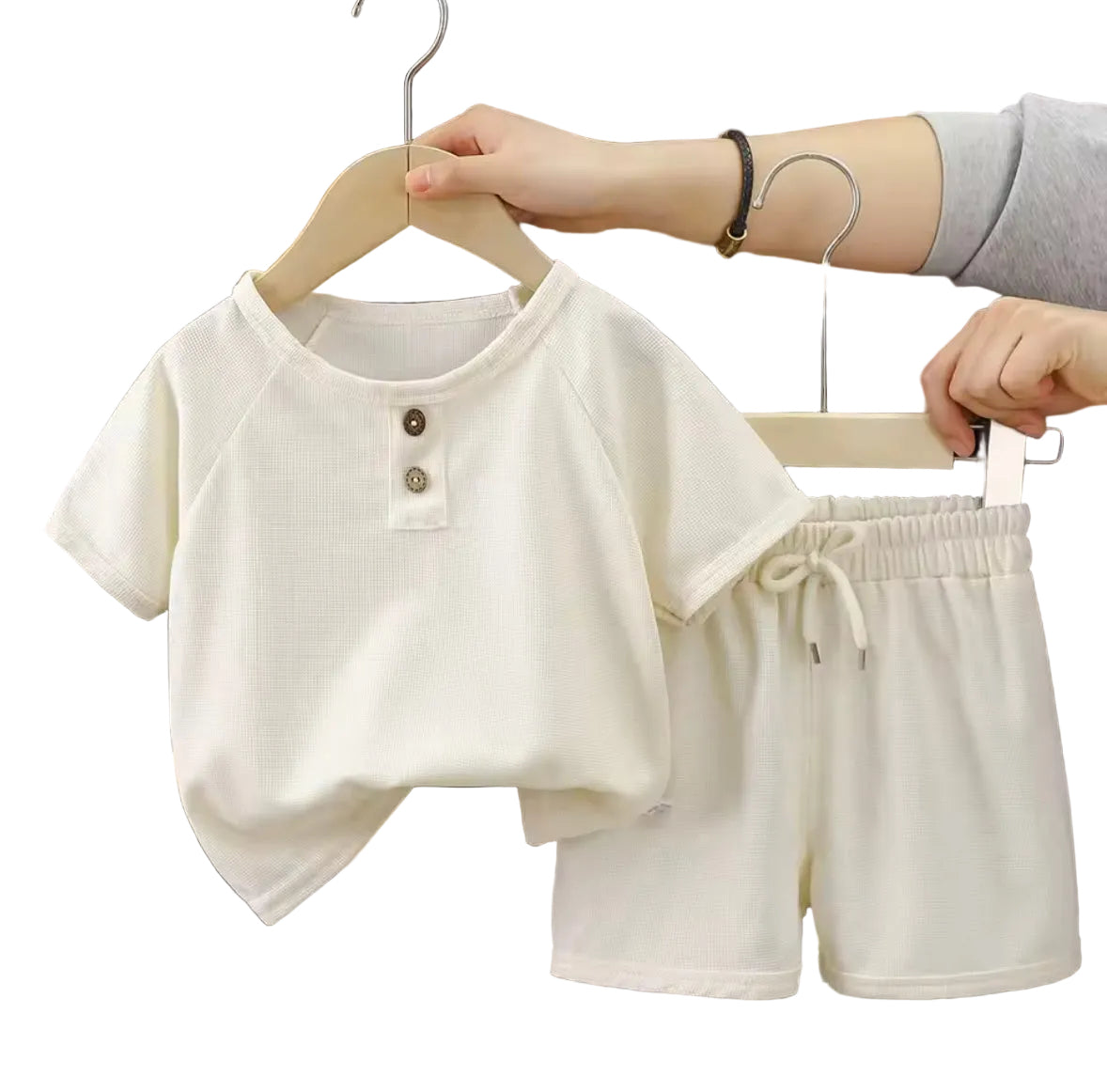 Children's white outfit with a shirt and shorts on hangers against a neutral background.
