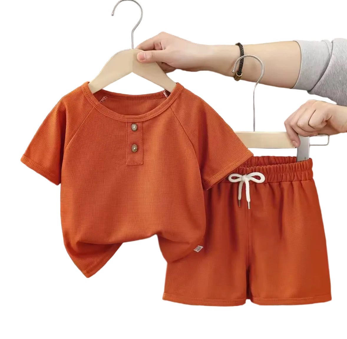 Children's orange shirt and shorts set on hangers against a dark curtain background.