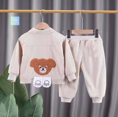 Children's corduroy outfit with teddy bear design on a hanger against a gray curtain background.