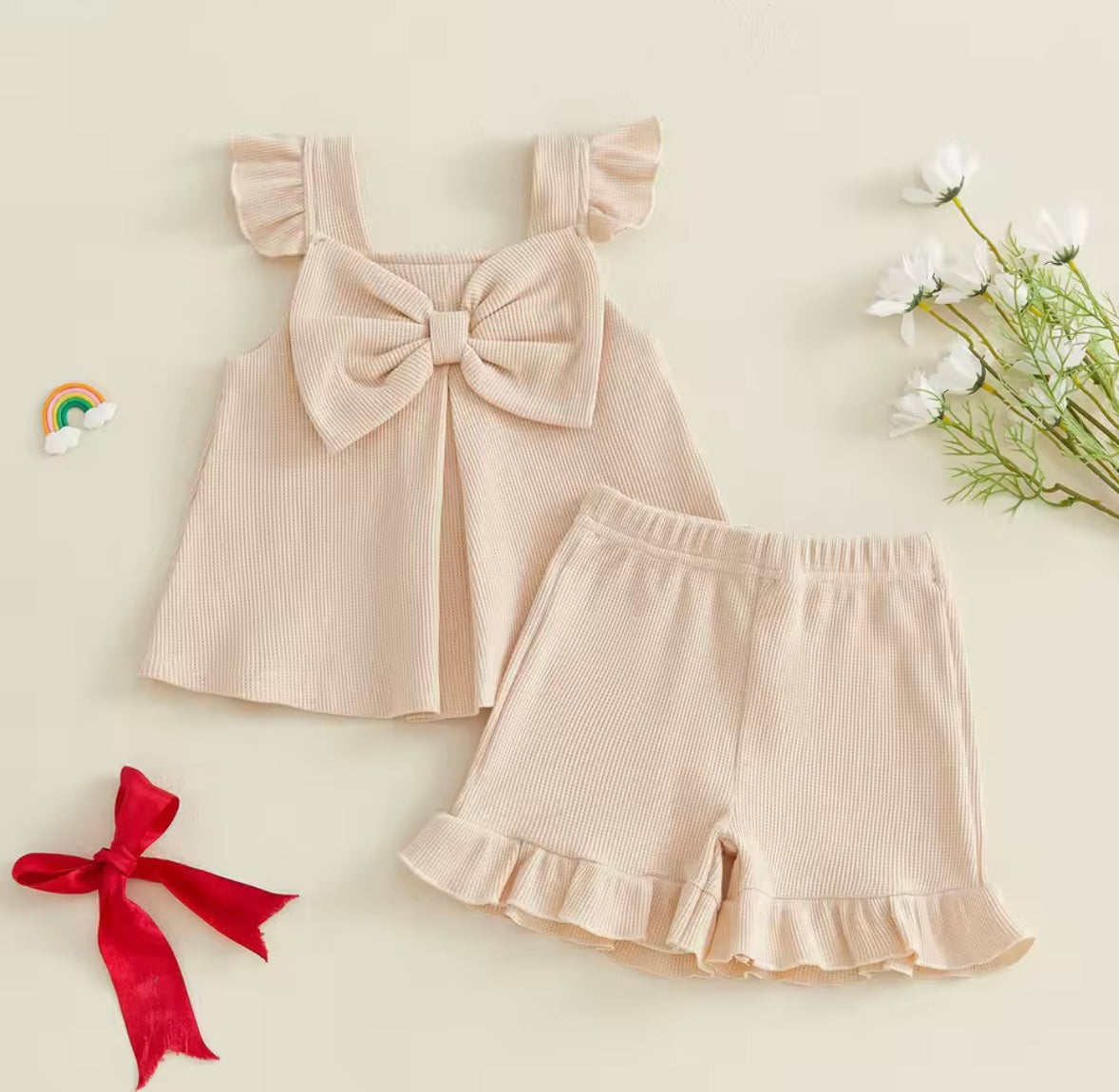 Beige ribbed dress with a large bow and matching shorts on a light background with decorative elements.