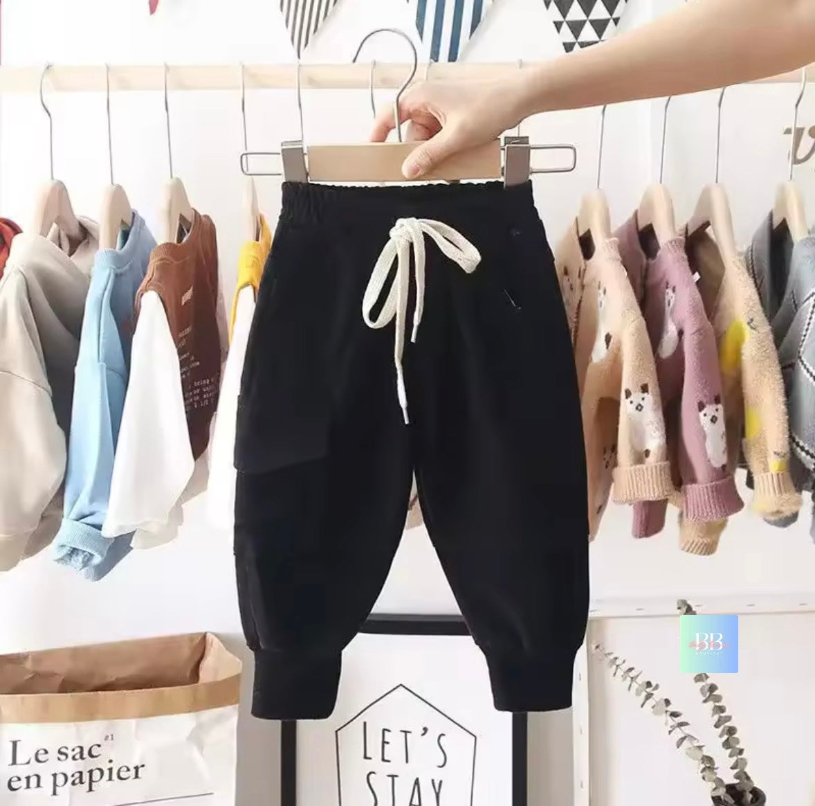 Black harem pants with a white drawstring on a hanger against a background of children's clothes.