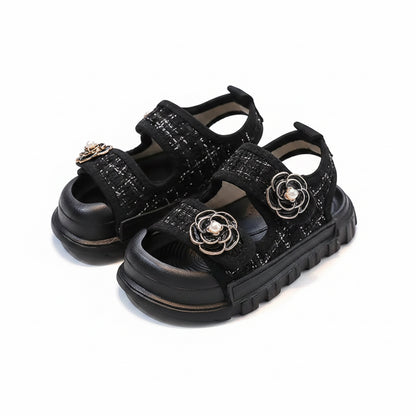 Black sandals with floral embellishments on a light gray background