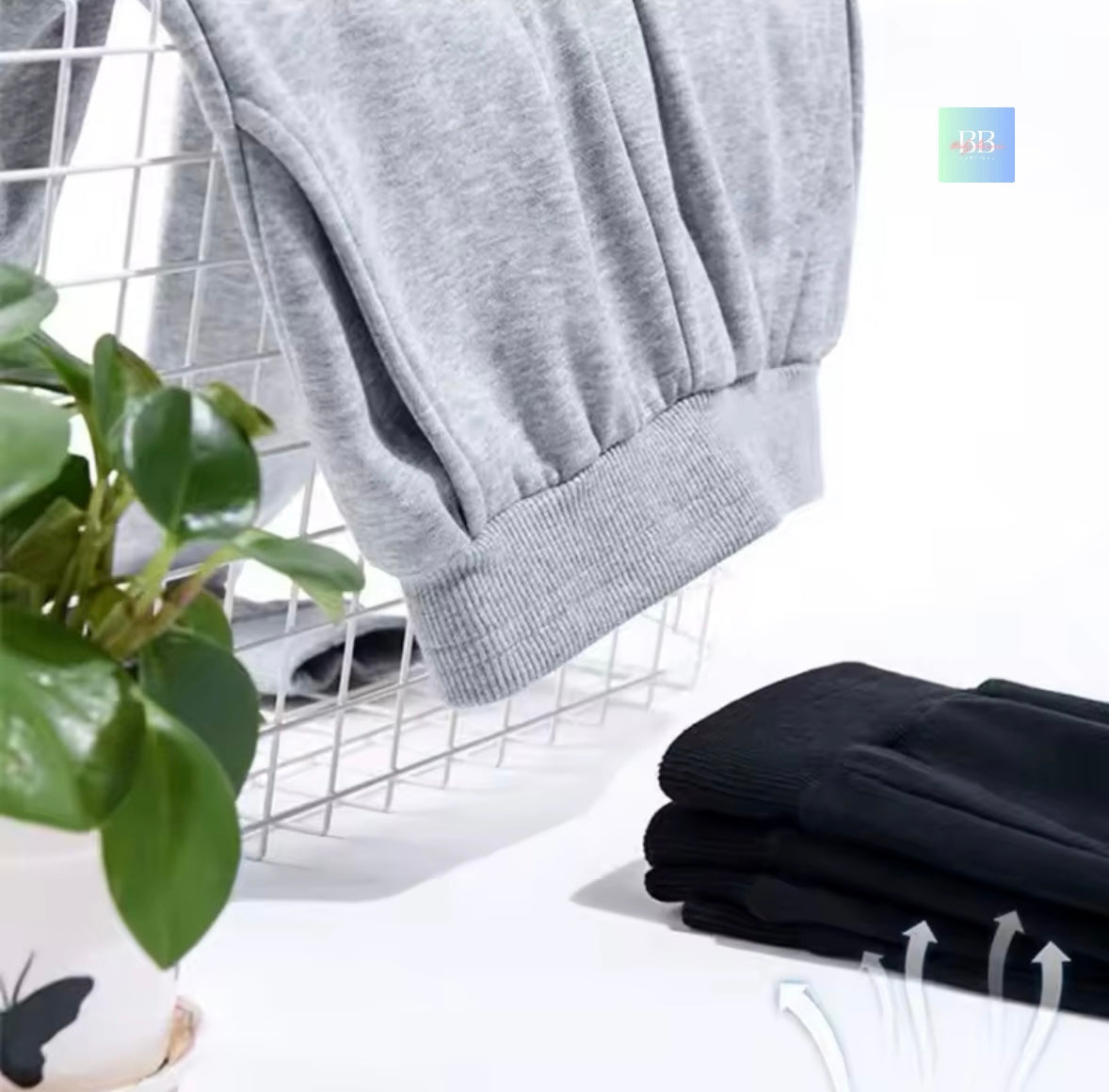 Gray sweatshirt hanging on a white rack with black gloves and a plant in the foreground.