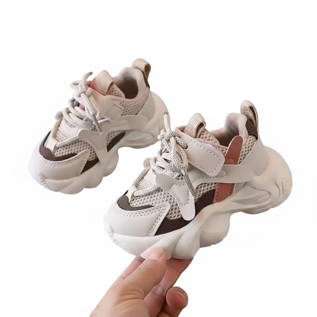 Pair of children's sneakers on a gray surface with a hand holding one shoe.