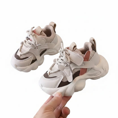Pair of children's sneakers on a gray surface with a hand holding one shoe.