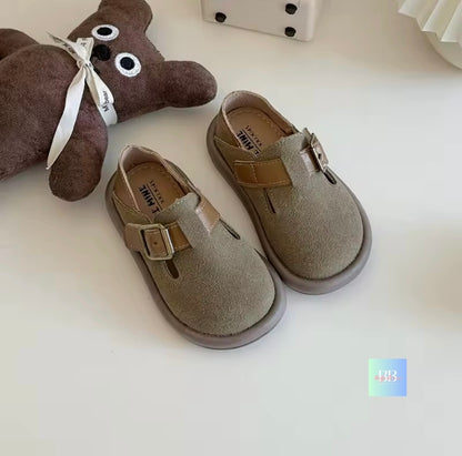 Pair of children's shoes with a brown teddy bear toy on a light background