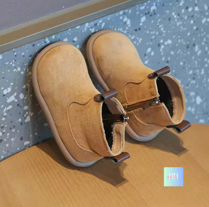 Pair of tan children's boots on a wooden surface with a speckled gray wall in the background.