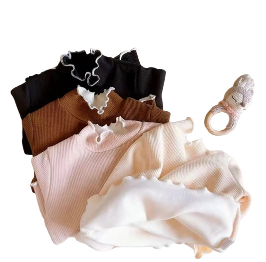 Set of ruffled tops in black, brown, and beige on a textured surface with teddy bears in the background.